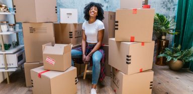 A smiling woman sitting between two piles of packed moving boxes.