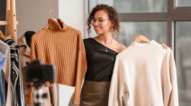 A woman holding up two sweaters, making a fashion video.